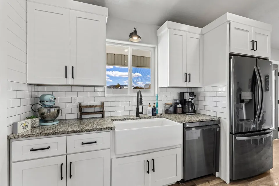 Kitchen with stainless steel fridge with ice dispenser, white cabinets, and dark stone counters