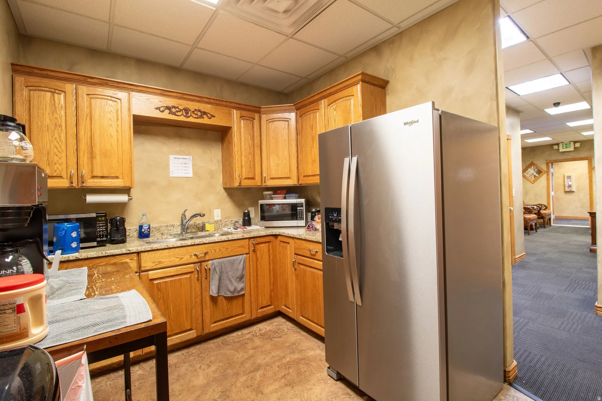 Kitchen with a drop ceiling, stainless steel appliances, wood finish cabinetry, and light stone counters