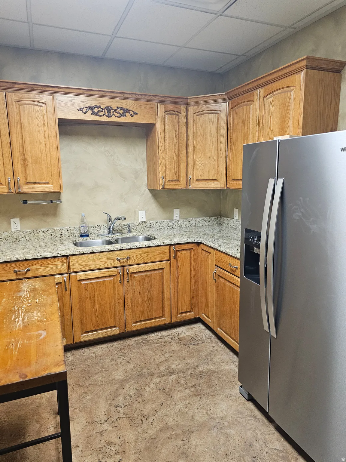Kitchen featuring oak cabinetry, granite-look countertops, a stainless steel refrigerator, a dual basin sink with a chrome faucet, and patterned flooring