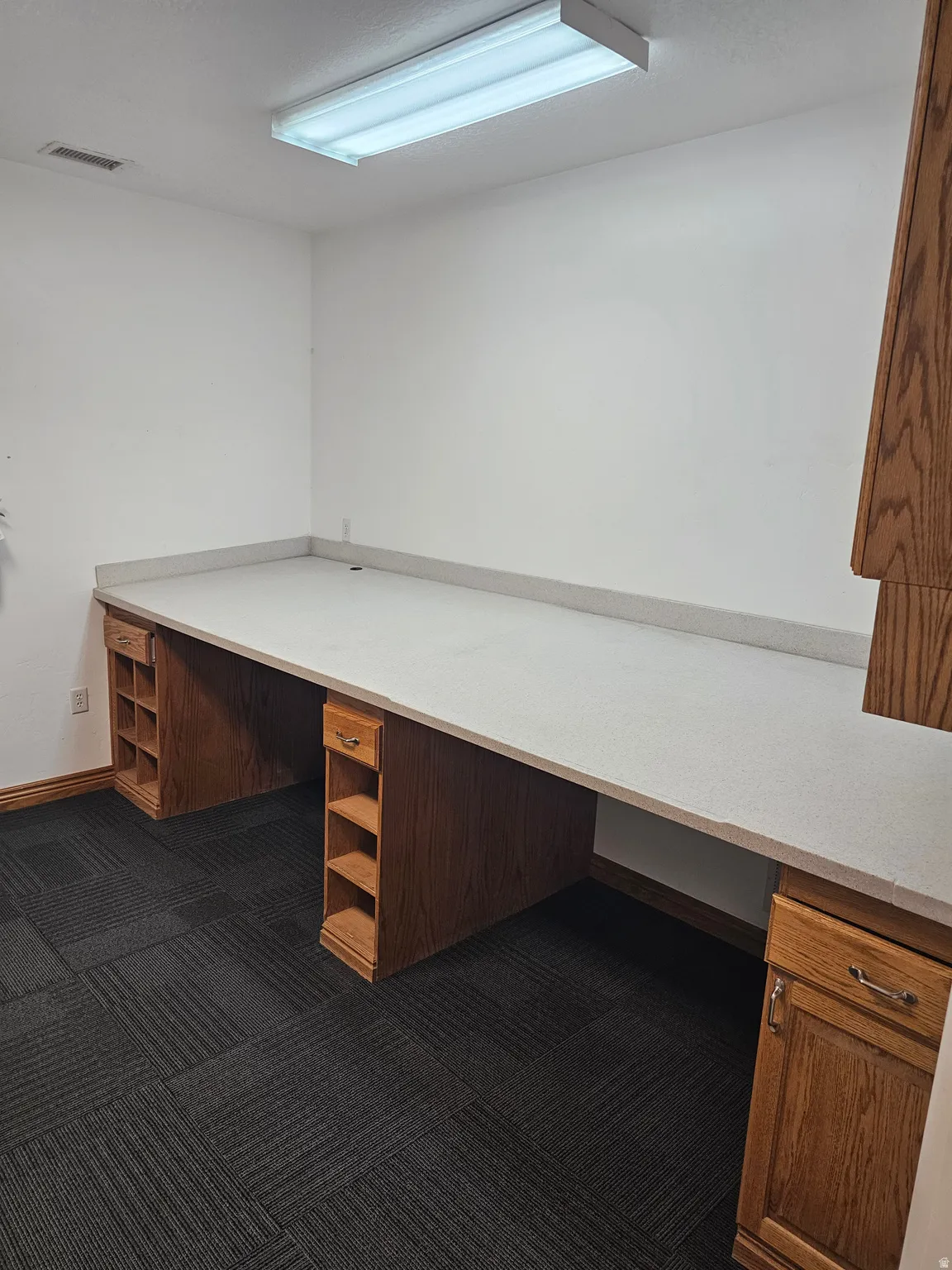 Expansive built-in desk with a light-toned countertop, integrated shelving, and wood-finish cabinetry