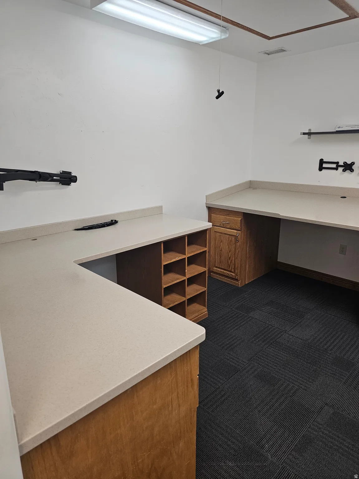 Spacious work area featuring extensive light-toned countertops, built-in wooden cabinetry, integrated shelving, and dark patterned carpet flooring
