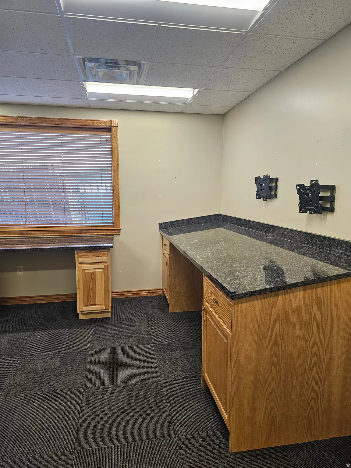 Dedicated workspace featuring built-in wood cabinetry, dark stone countertops, and a full window with wood blinds
