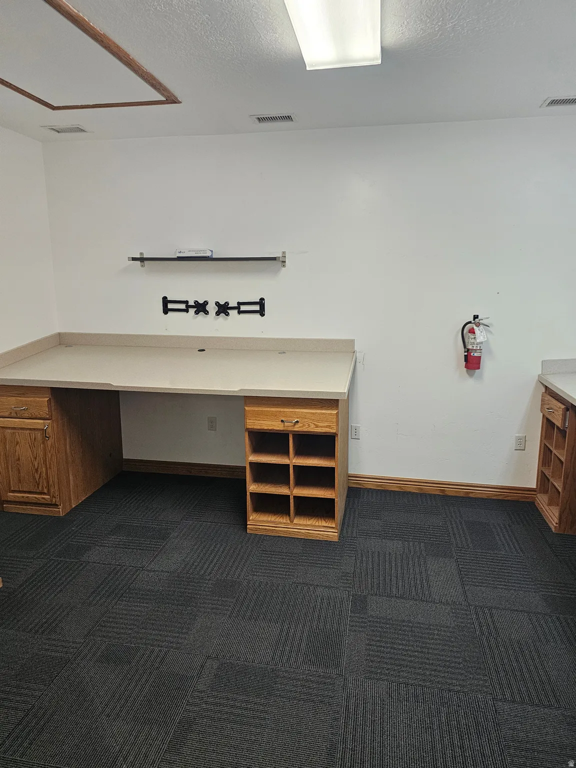Built-in oak cabinetry with a light-toned countertop, integrated shelving, and dark patterned carpet flooring
