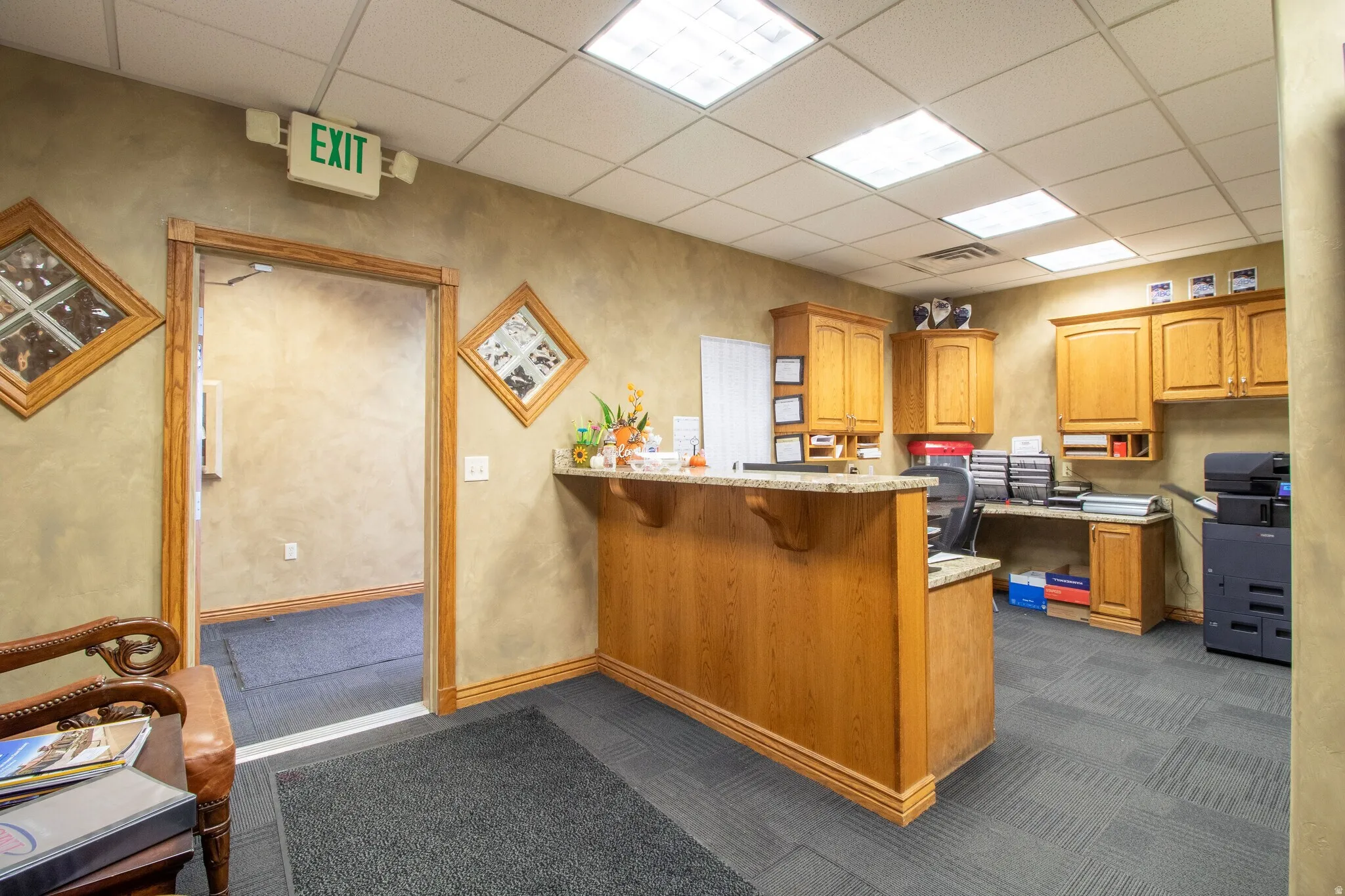 Kitchen featuring a drop ceiling, a peninsula, wood finish cabinetry, a breakfast bar, and light stone counters