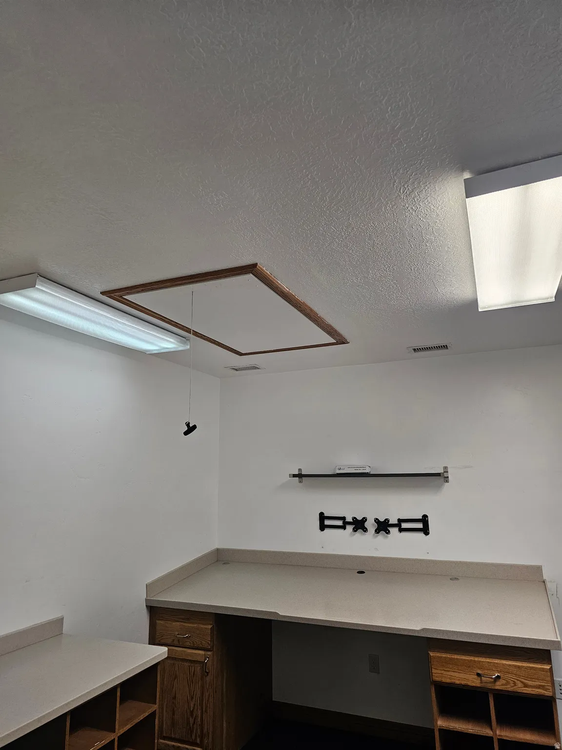 Room featuring built-in wood-finish cabinetry, light-toned countertops, and multiple fluorescent ceiling light fixtures