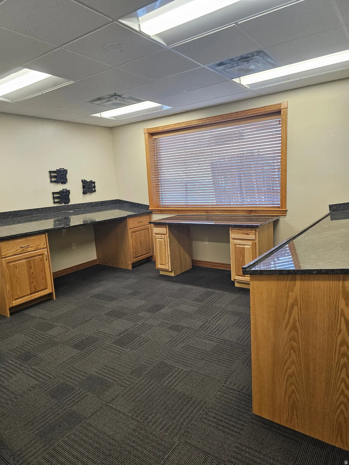 Dedicated workspace featuring built-in oak cabinetry, dark speckled countertops, and a large window with blinds