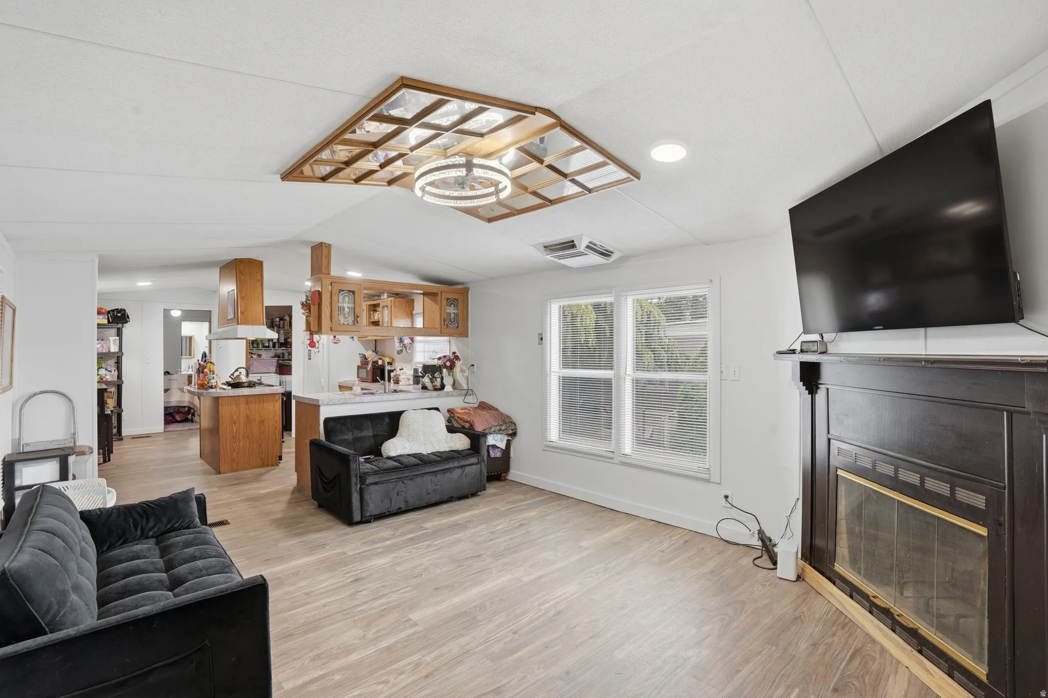 Living room featuring light wood-type flooring, a glass covered fireplace, and recessed lighting