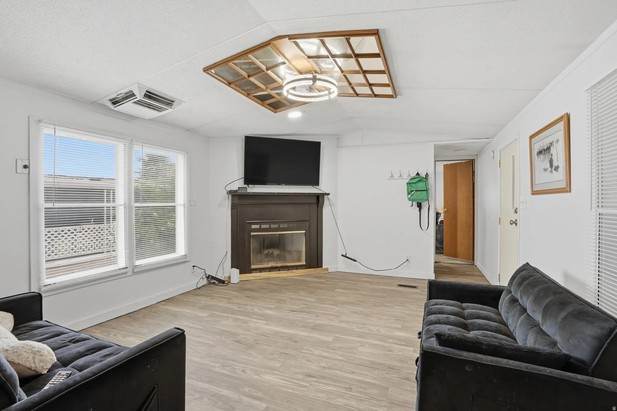 Living room with light wood finished floors, lofted ceiling, and a glass covered fireplace