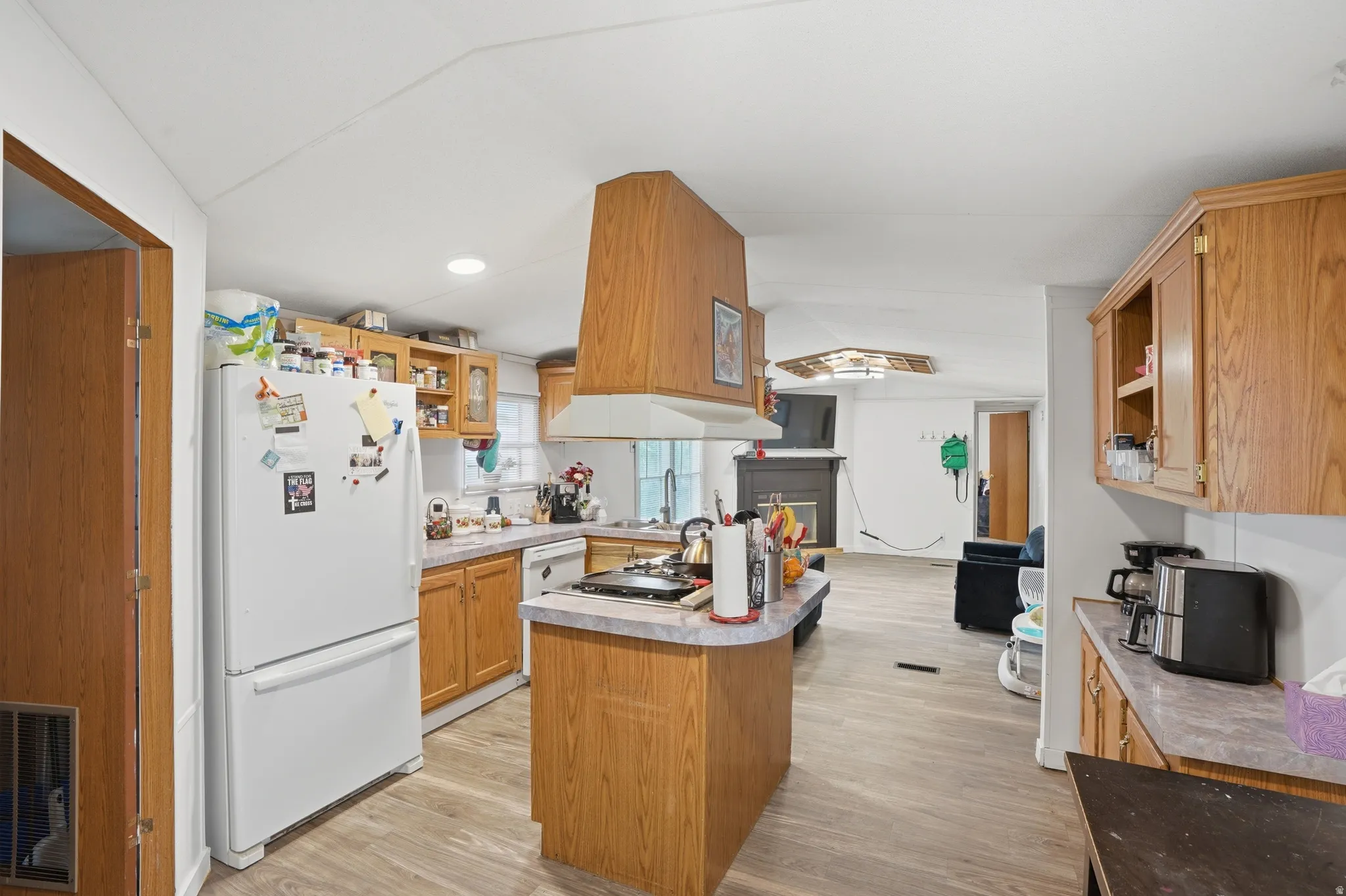 Kitchen with freestanding refrigerator, light wood-style flooring, light countertops, wood finish cabinets, and a center island