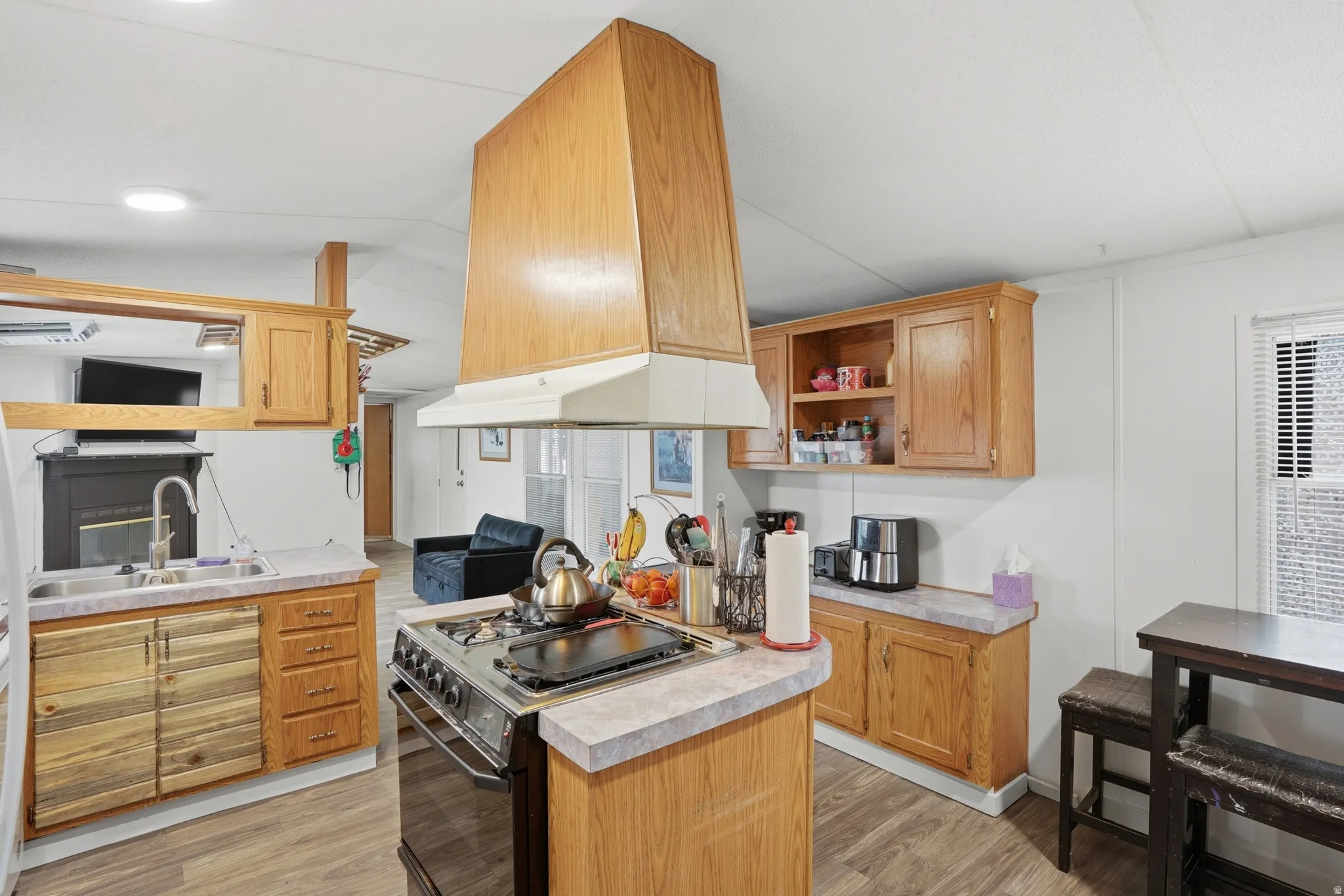 Kitchen with open shelves, black electric range, light countertops, light wood-style floors, and lofted ceiling