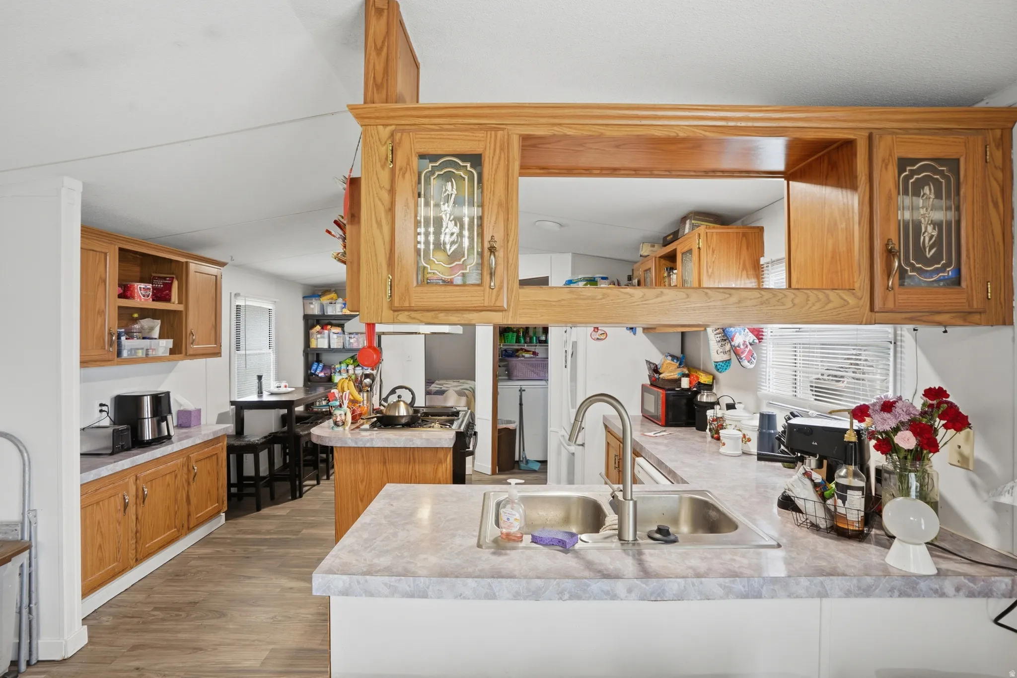 Kitchen with wood finish cabinets, a peninsula, light countertops, open shelves, and dark wood-style floors