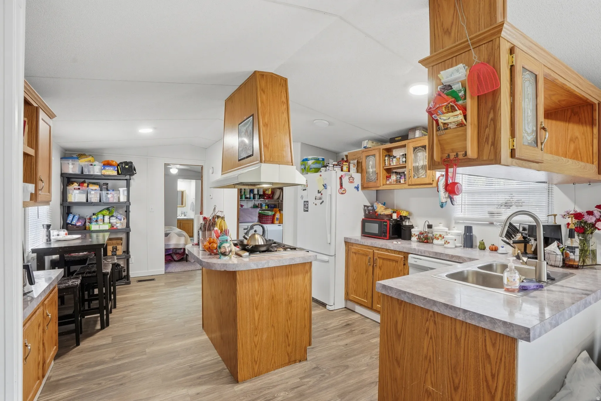 Kitchen featuring wood finish cabinetry, vaulted ceiling, light wood-style floors, a peninsula, and freestanding refrigerator