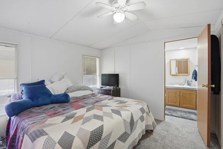 Bedroom with lofted ceiling, a ceiling fan, light colored carpet, and ensuite bathroom