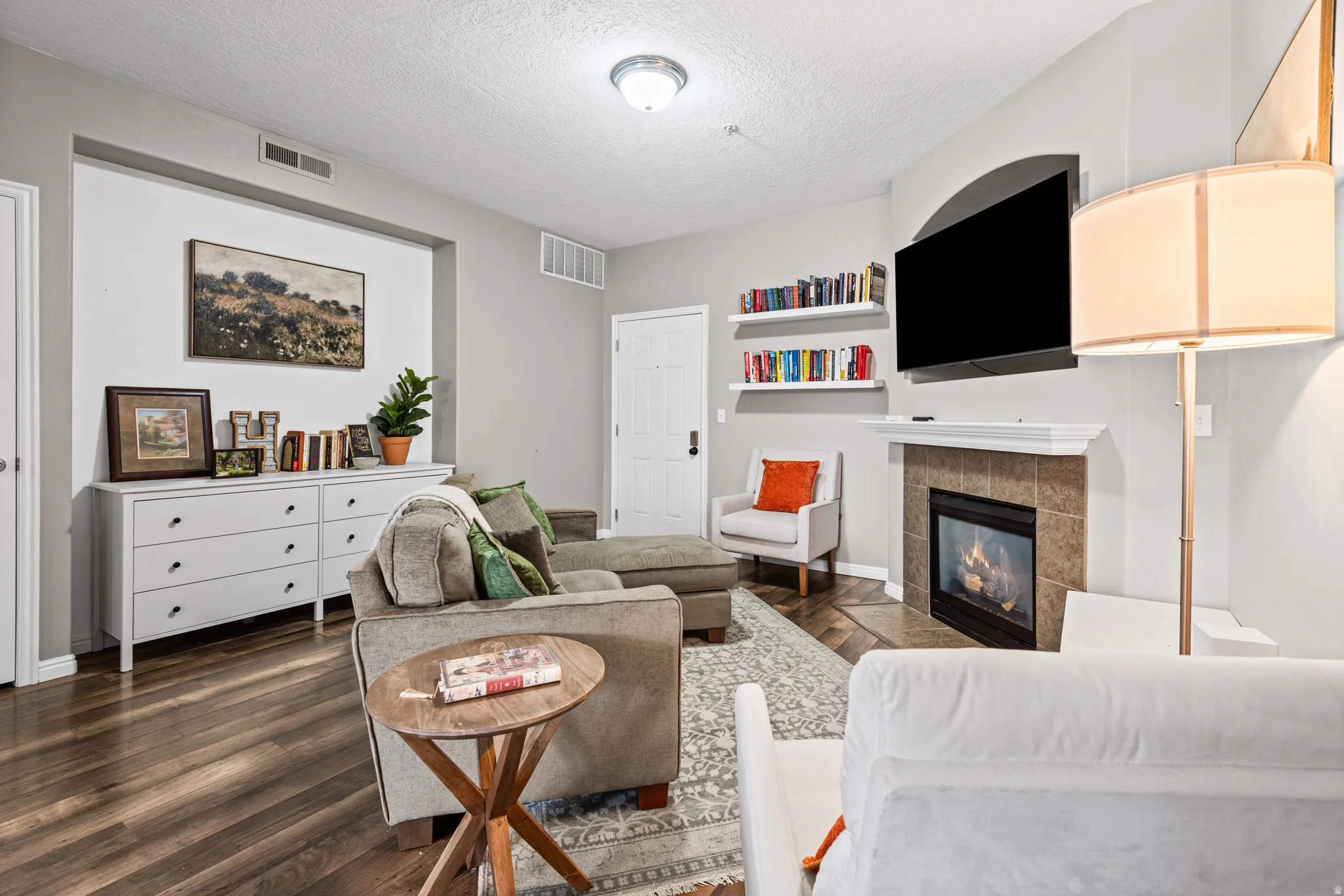 Living area with dark wood-style flooring, a tiled fireplace, and a textured ceiling