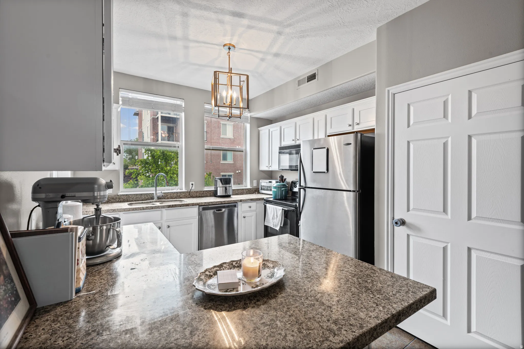 Kitchen with a peninsula, black appliances, dark stone countertops, white cabinetry, and a chandelier