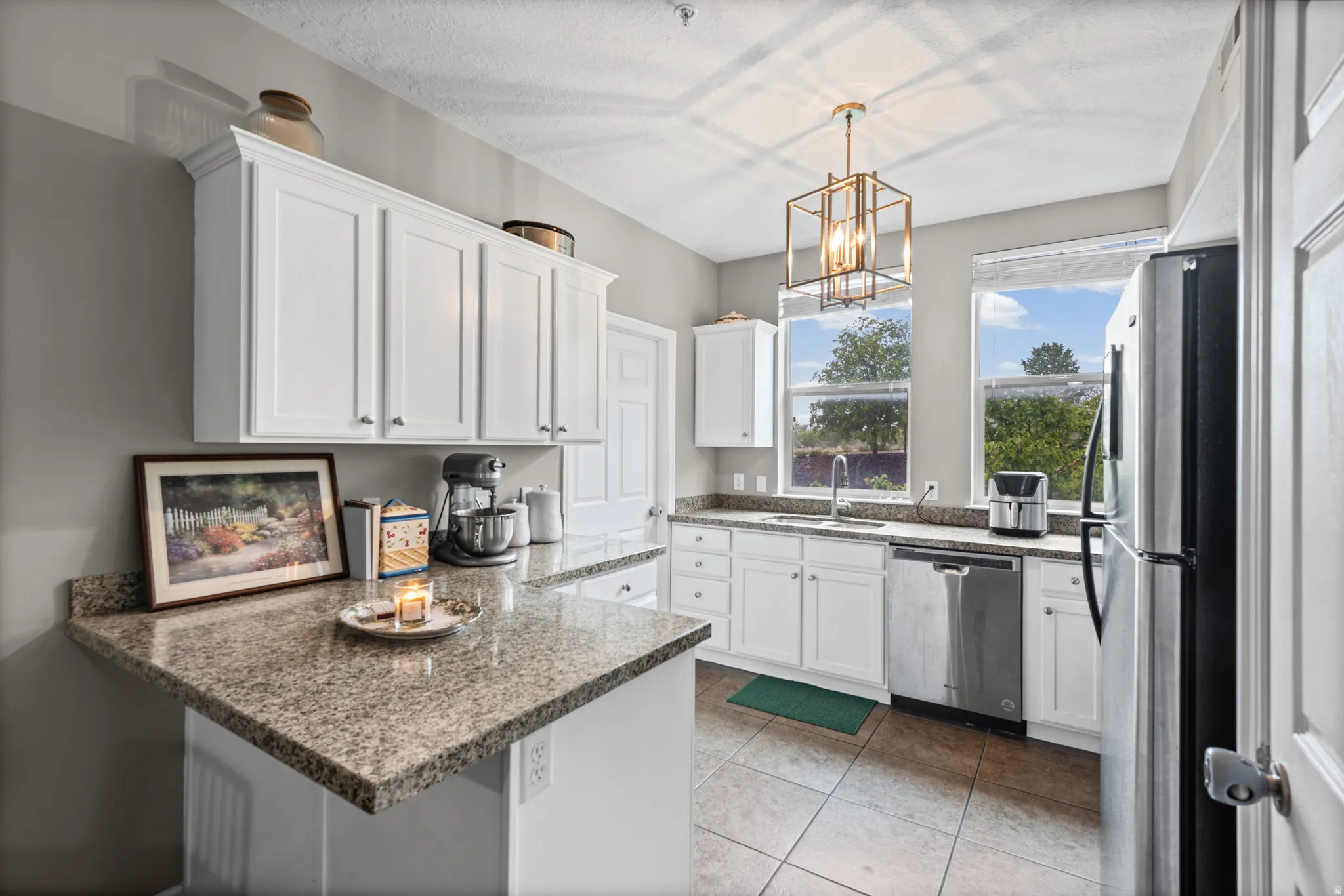 Kitchen featuring a peninsula, white cabinetry, stainless steel appliances, light stone counters, and a chandelier