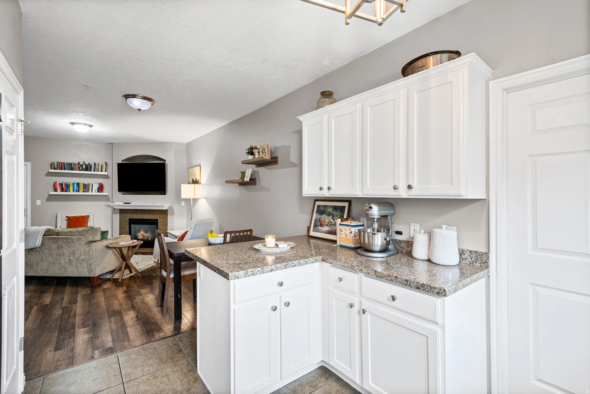 Kitchen featuring white cabinets, open floor plan, dark tile patterned flooring, a peninsula, and a tiled fireplace