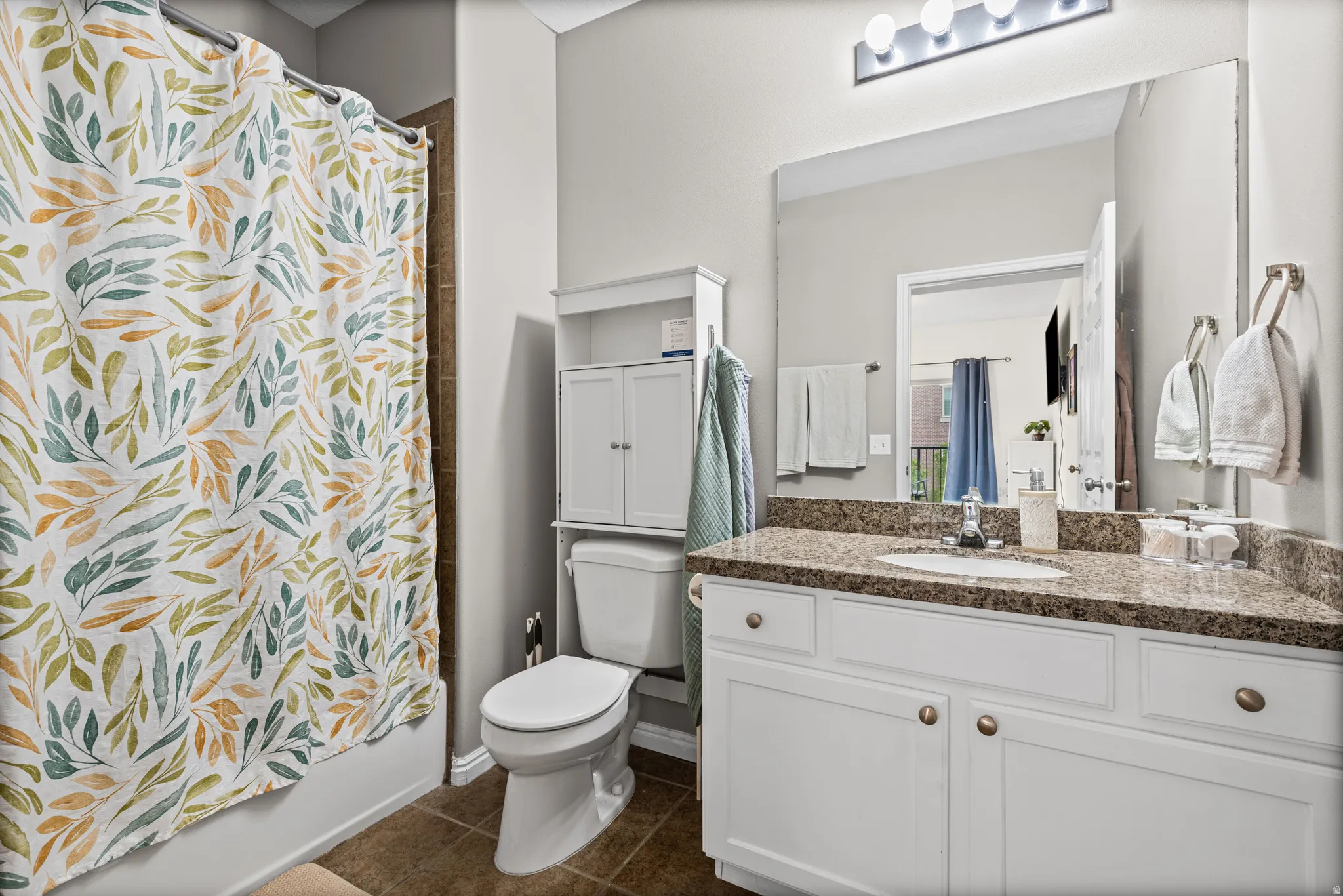 Full bathroom featuring vanity, shower / bath combo with shower curtain, and dark tile patterned flooring