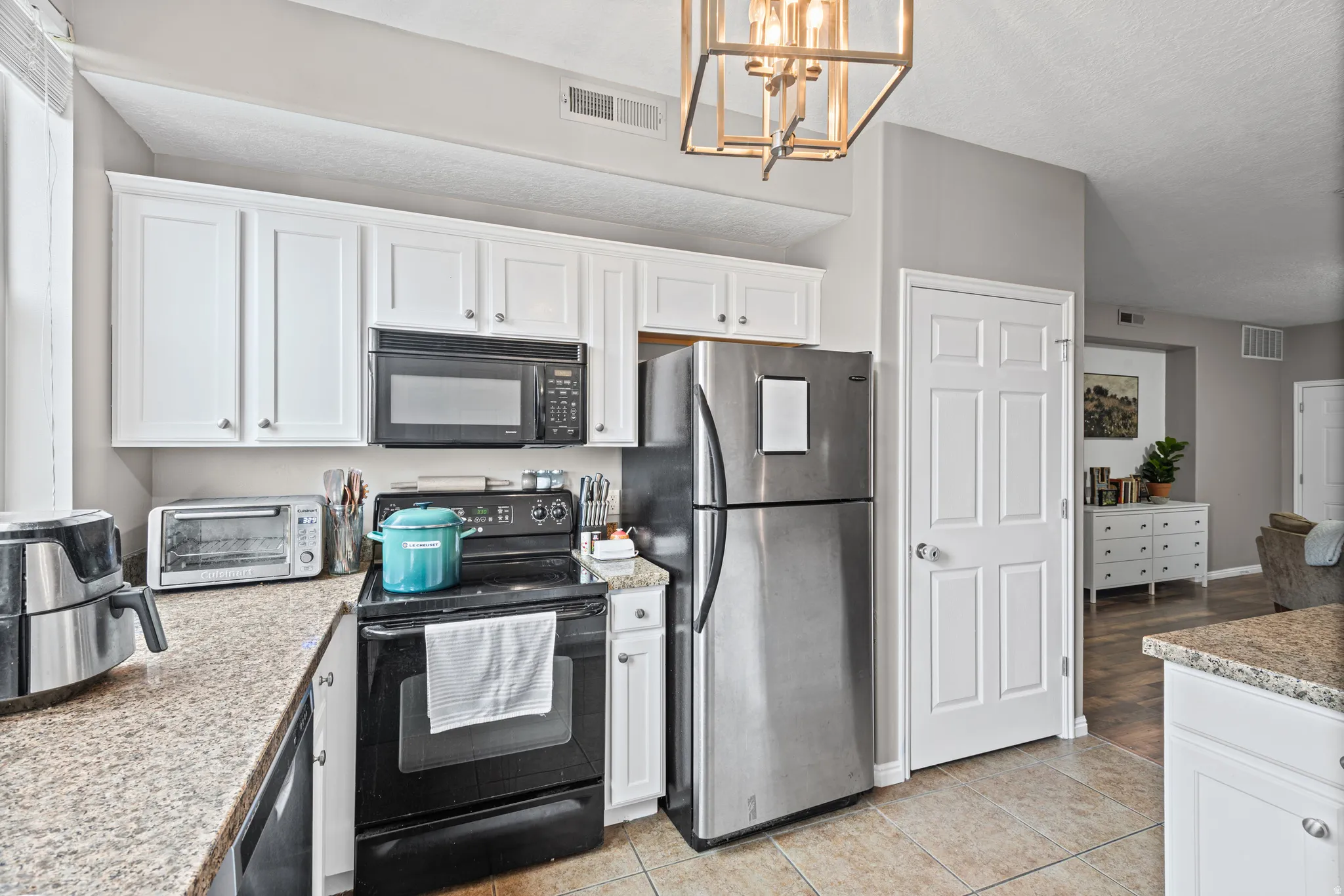 Kitchen featuring black appliances, white cabinetry, light countertops, and a textured ceiling