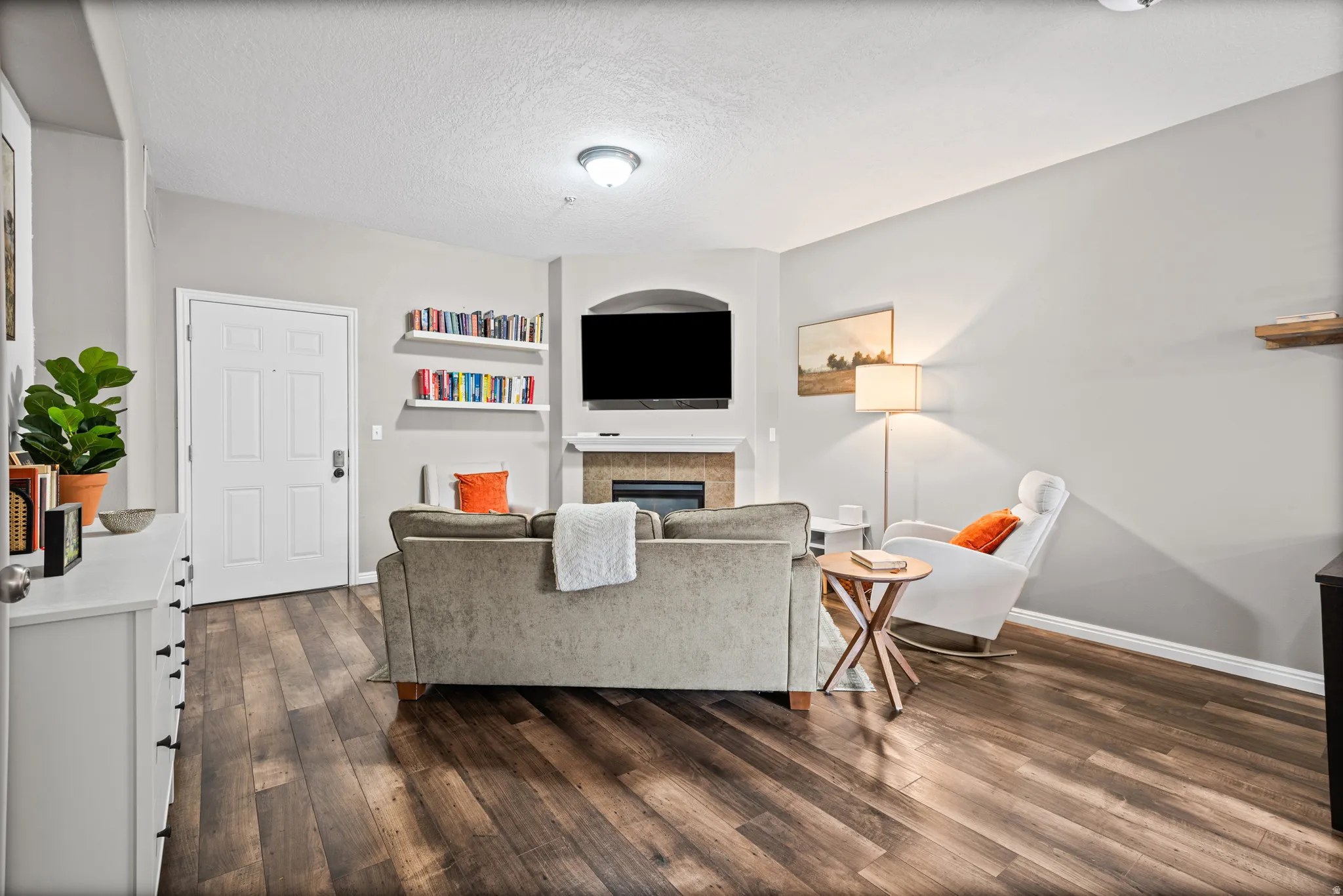 Living room featuring a textured ceiling, dark wood finished floors, a glass covered fireplace, and built in shelves