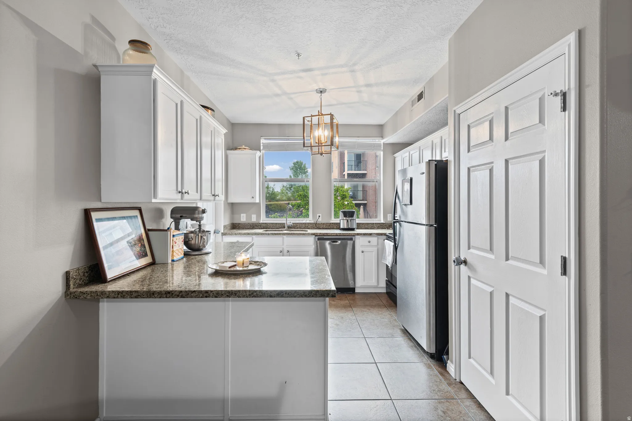 Kitchen with stainless steel appliances, white cabinetry, suspended lighting, a peninsula, and a textured ceiling