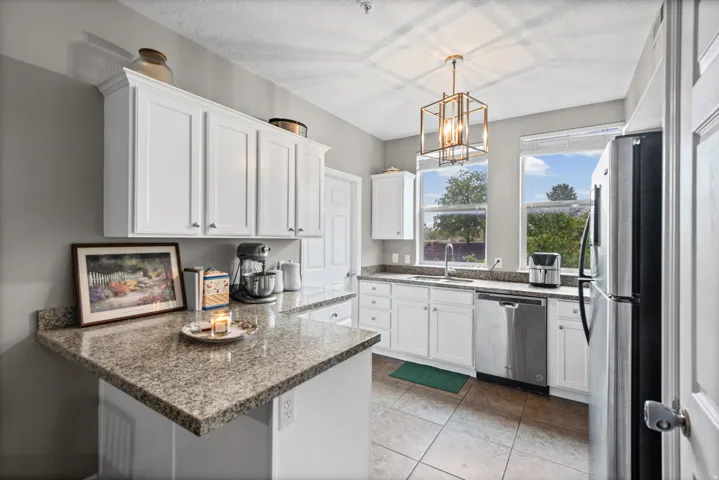 Kitchen featuring a peninsula, white cabinetry, stainless steel appliances, light stone counters, and a chandelier