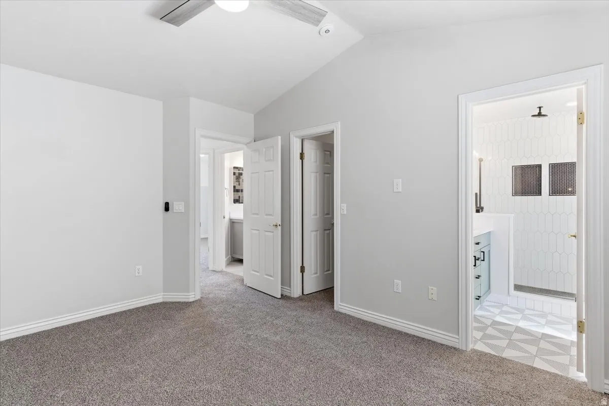 Unfurnished bedroom featuring light carpet, vaulted ceiling, ensuite bath, a ceiling fan, and a closet