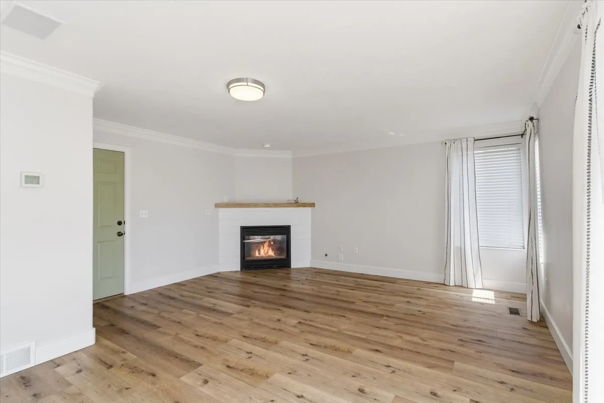 Unfurnished living room with ornamental molding, light wood-style flooring, and a glass covered fireplace