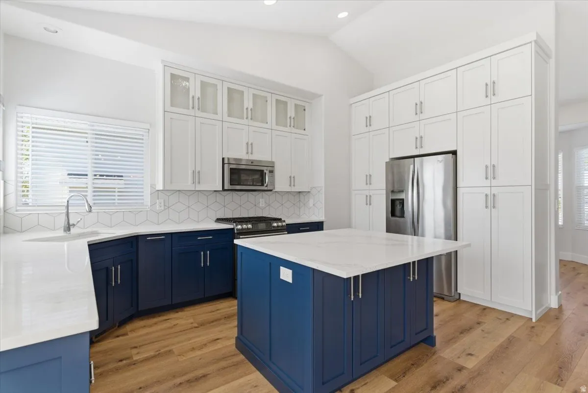 Two tone kitchen featuring glass insert cabinets, dual tone cabinetry, vaulted ceiling, stainless steel appliances, and light stone counters