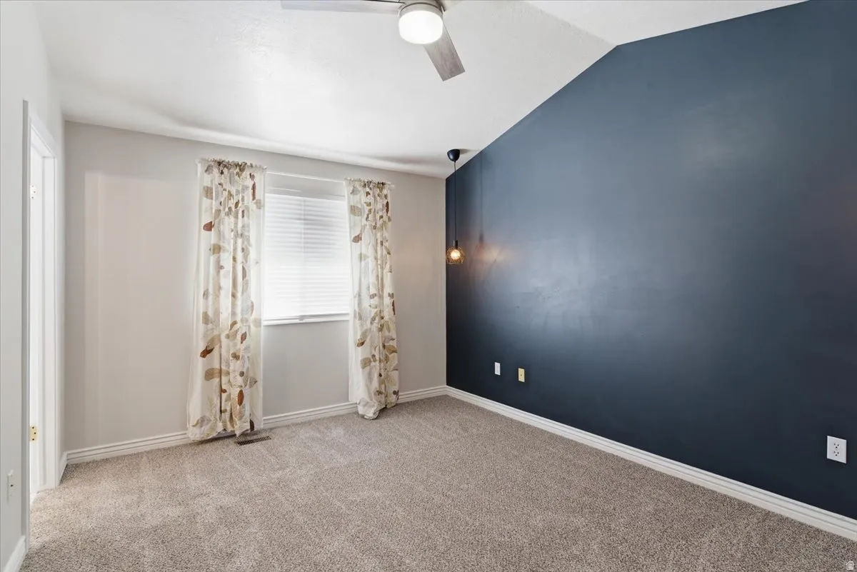 Spare room featuring light carpet, lofted ceiling, and ceiling fan
