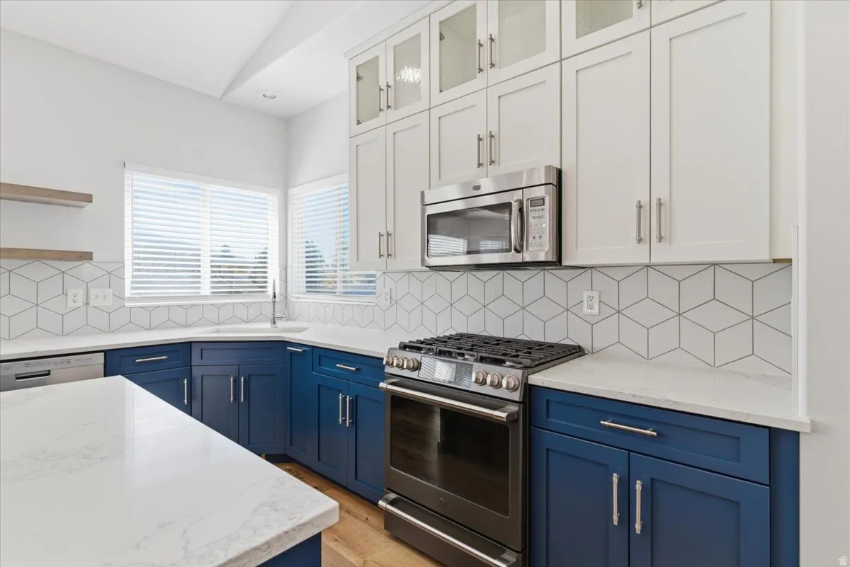 Dual tone kitchen with stainless steel appliances, light stone countertops, glass fronted cabinets, open shelves, and two tone cabinetry