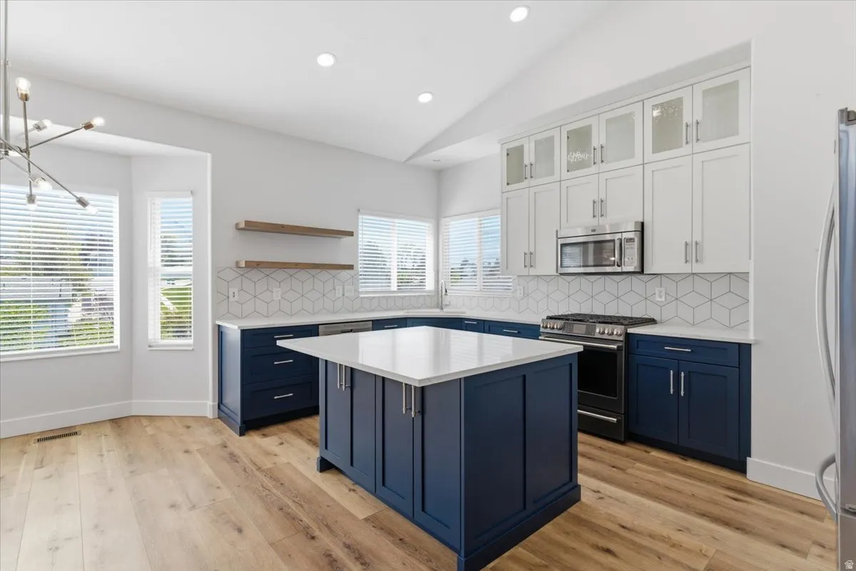 Kitchen featuring vaulted ceiling, glass fronted cabinets, decorative backsplash, stainless steel appliances, and a center island