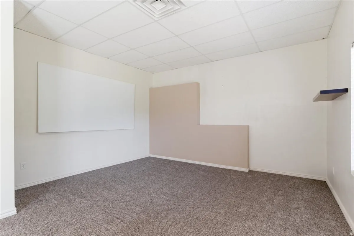 Carpeted empty room featuring a paneled ceiling and baseboards