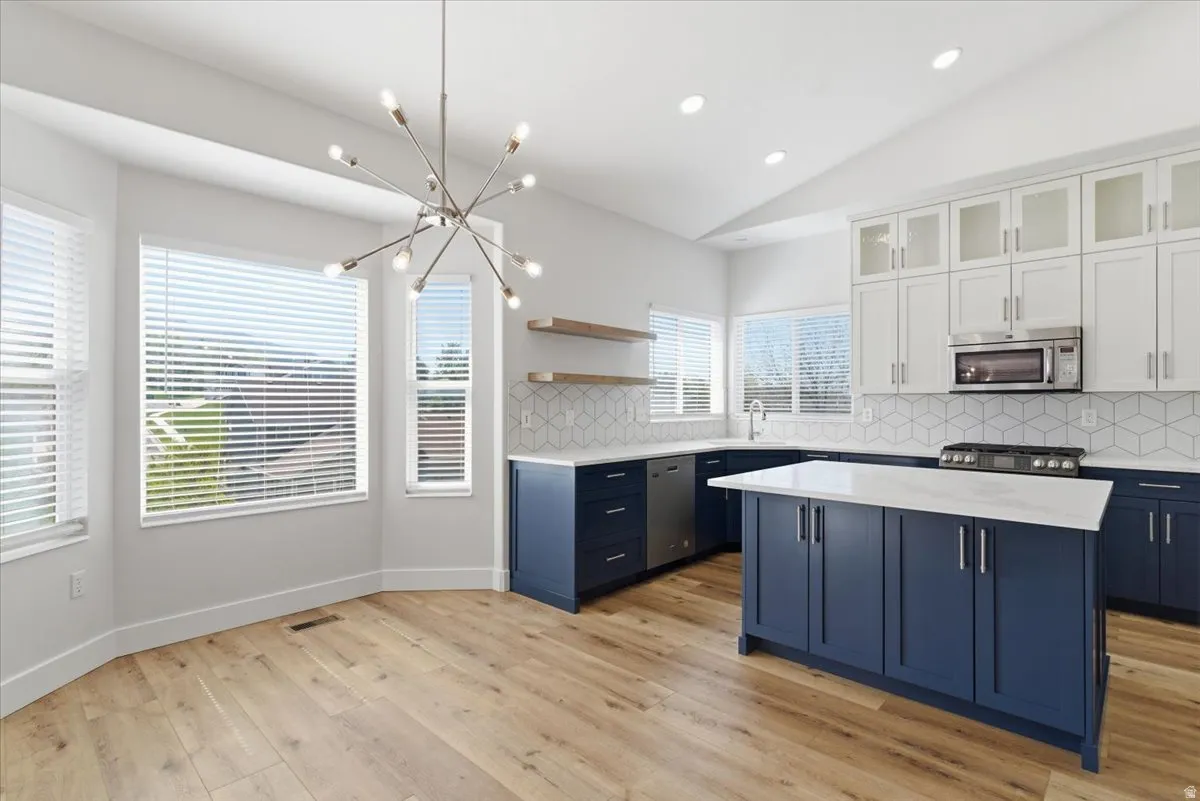 Kitchen with lofted ceiling, glass insert cabinets, backsplash, open shelves, and a kitchen island