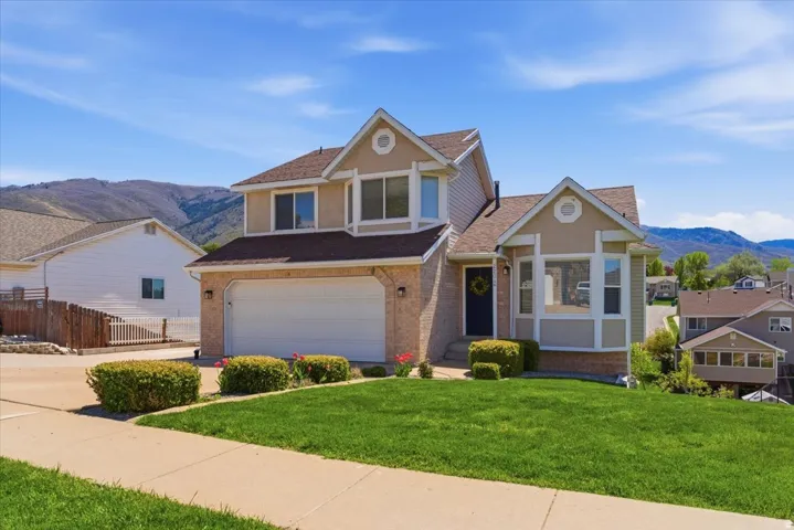 View of front facade with a mountain view, a garage, a shingled roof, brick siding, and driveway