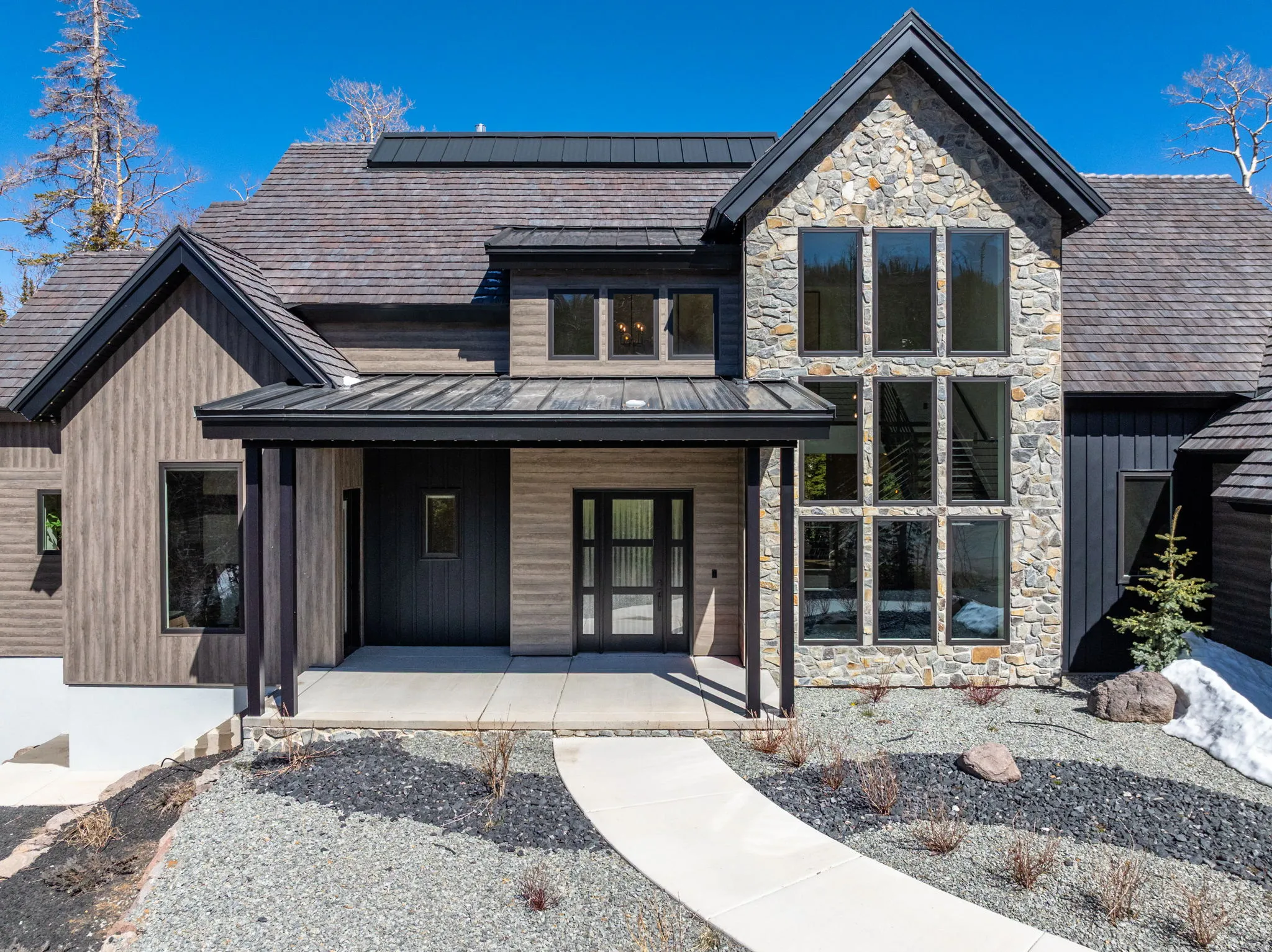View of front of property with covered porch, stone siding, solar panels, and a standing seam roof