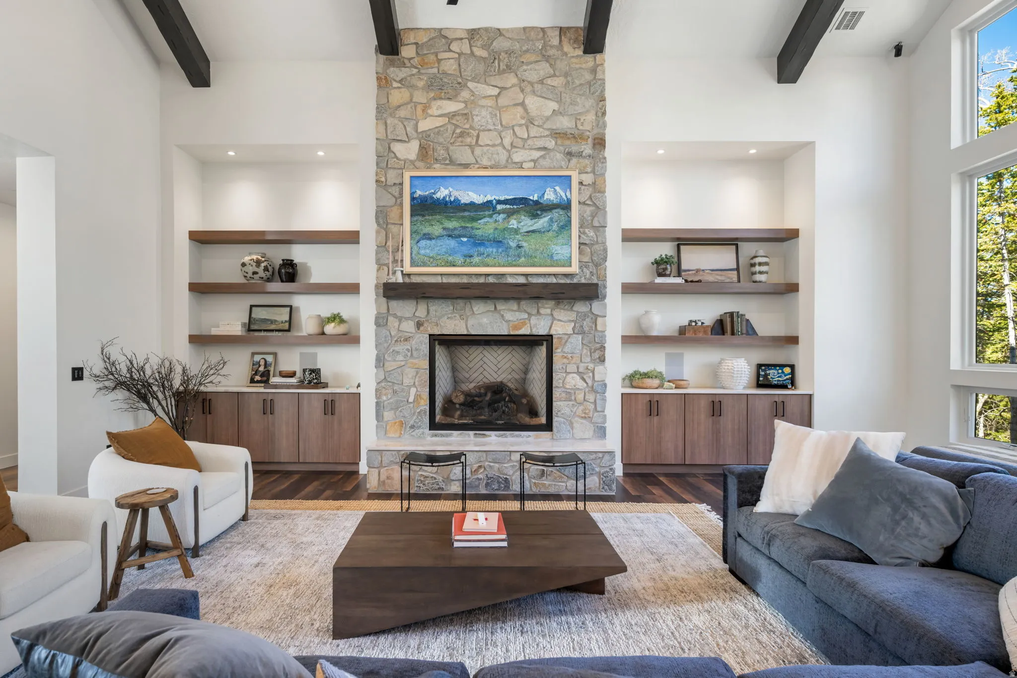 Living room with a stone fireplace, wood finished floors, and built in shelves