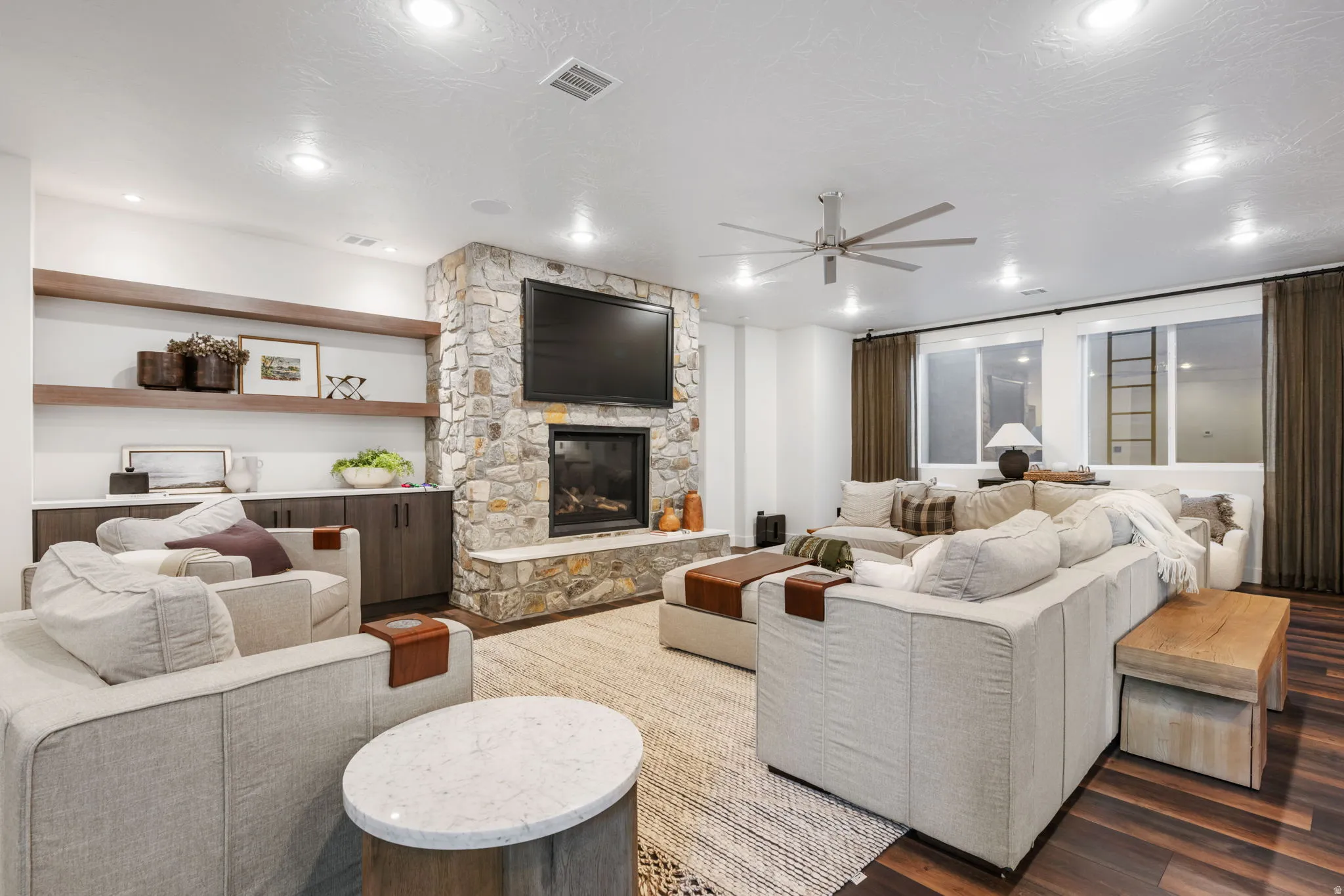 Living room with a ceiling fan, wood finished floors, a stone fireplace, and recessed lighting