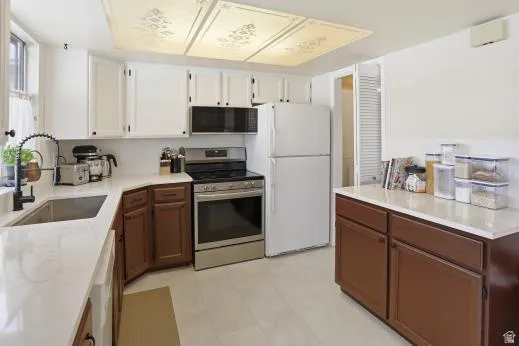Kitchen featuring electric range, dual tone cabinets, freestanding refrigerator, light flooring, and light stone counters