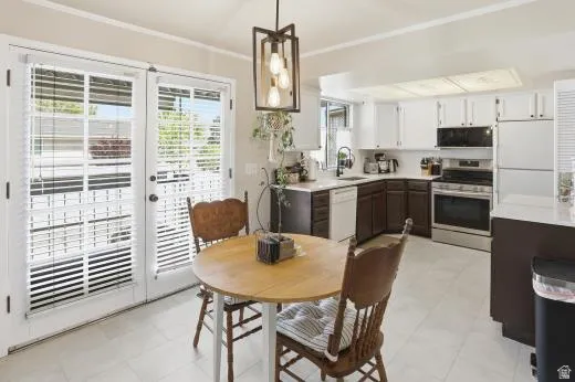 Kitchen featuring two tone cabinets, light countertops, white appliances, decorative light fixtures, and ornamental molding