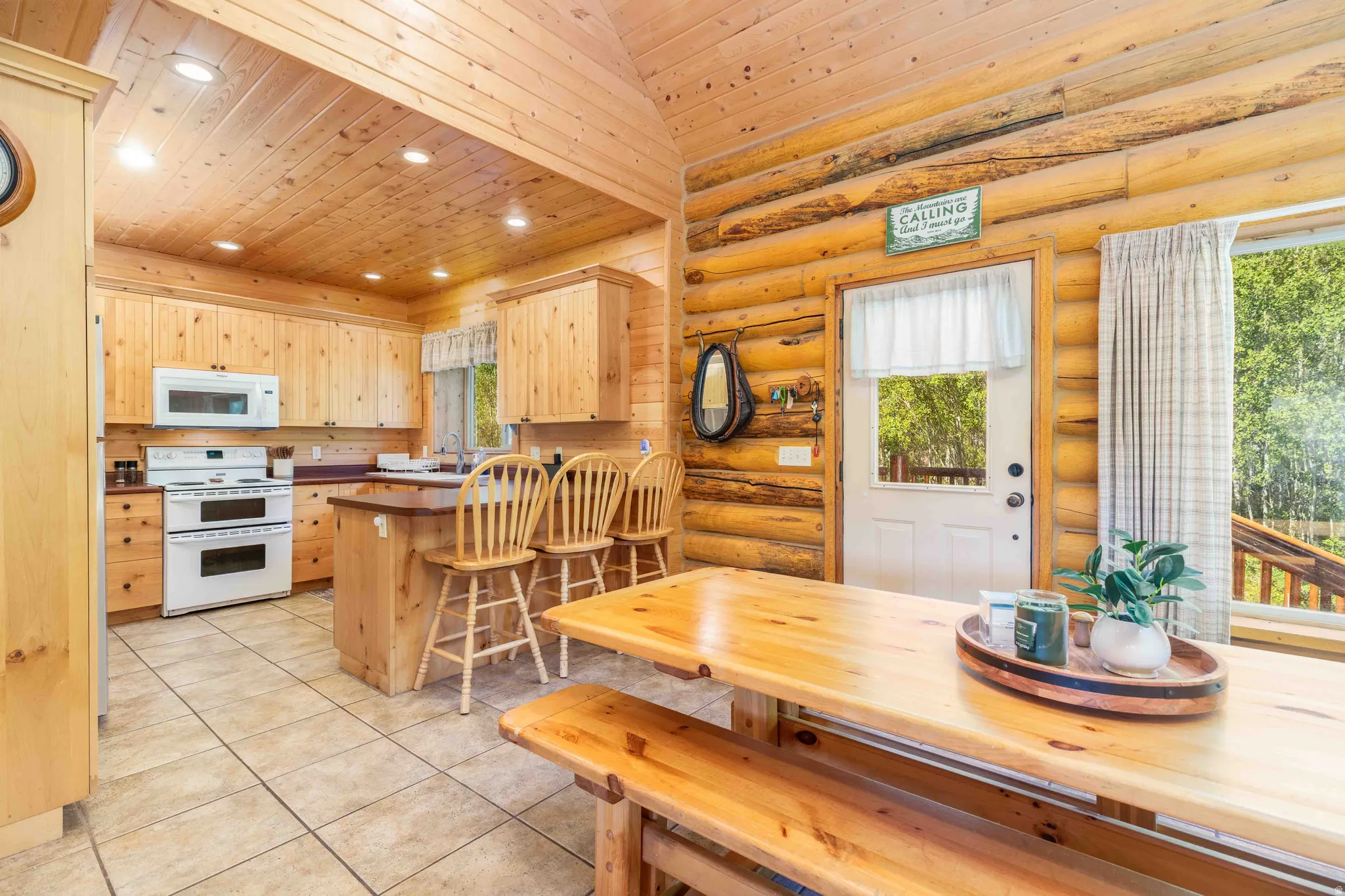 Kitchen with a breakfast bar area, light wood finish cabinets, wood ceiling, white appliances, and a peninsula