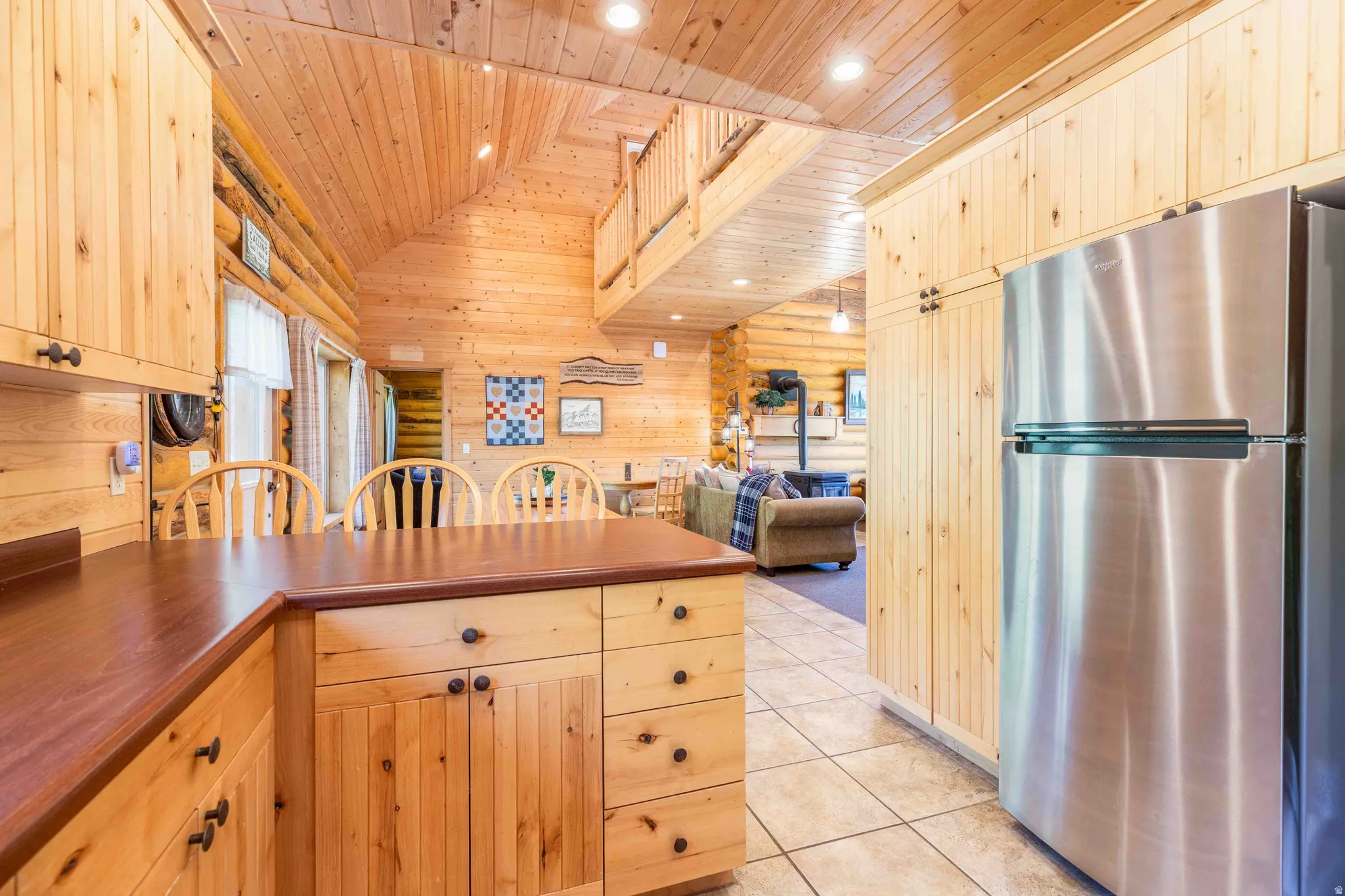 Kitchen featuring freestanding refrigerator, a vaulted wooden ceiling, light wood finish cabinets, rustic walls, and recessed lighting