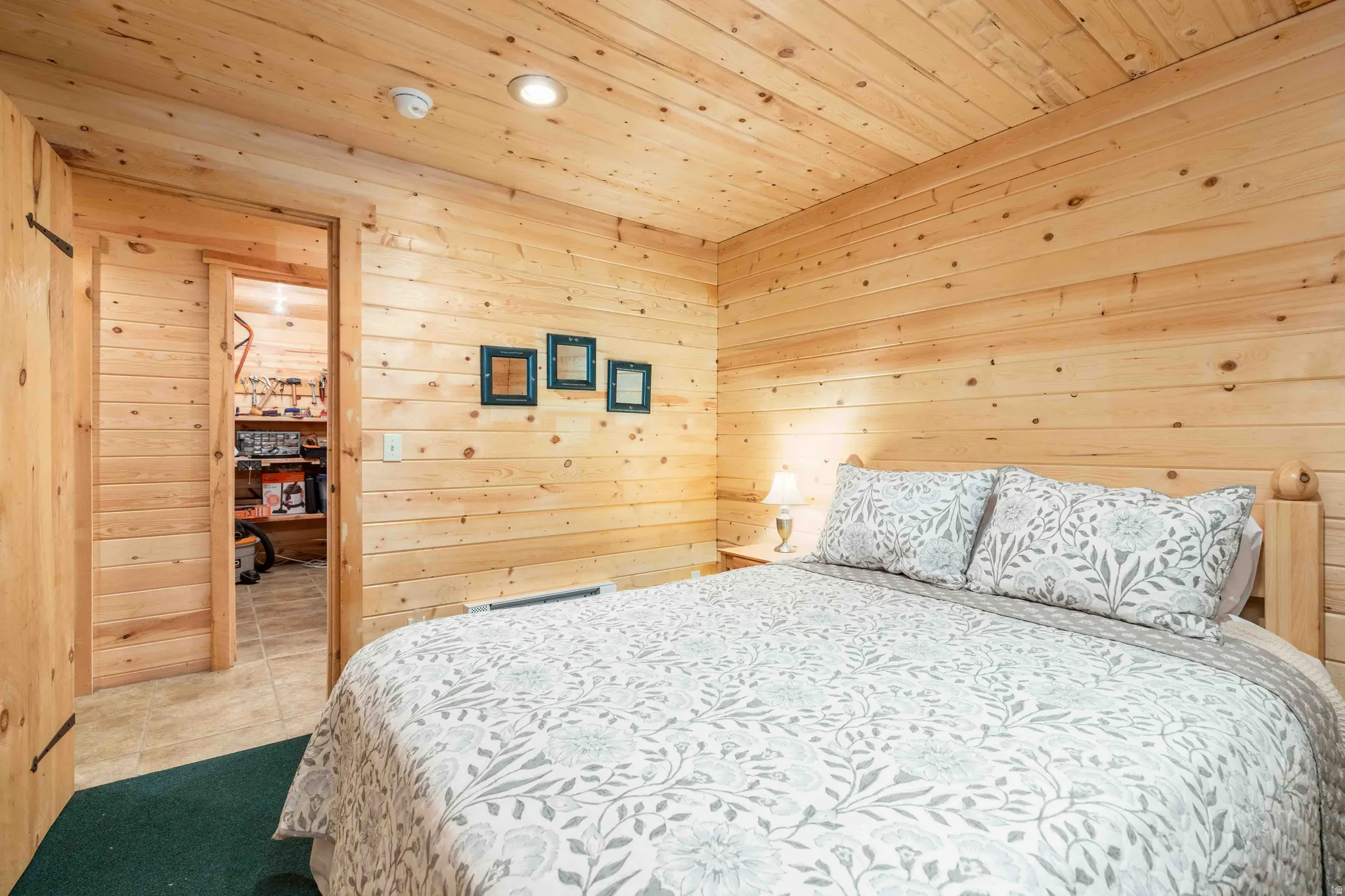 Bedroom with wooden walls, light tile patterned floors, wooden ceiling, baseboard heating, and recessed lighting