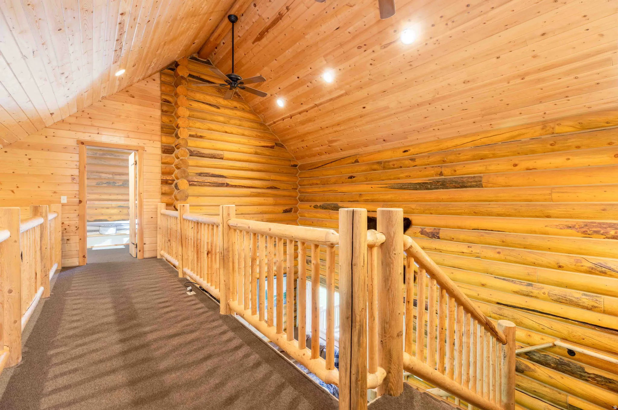 Hallway featuring an upstairs landing, a wooden ceiling with exposed beams, rustic walls, and dark colored carpet