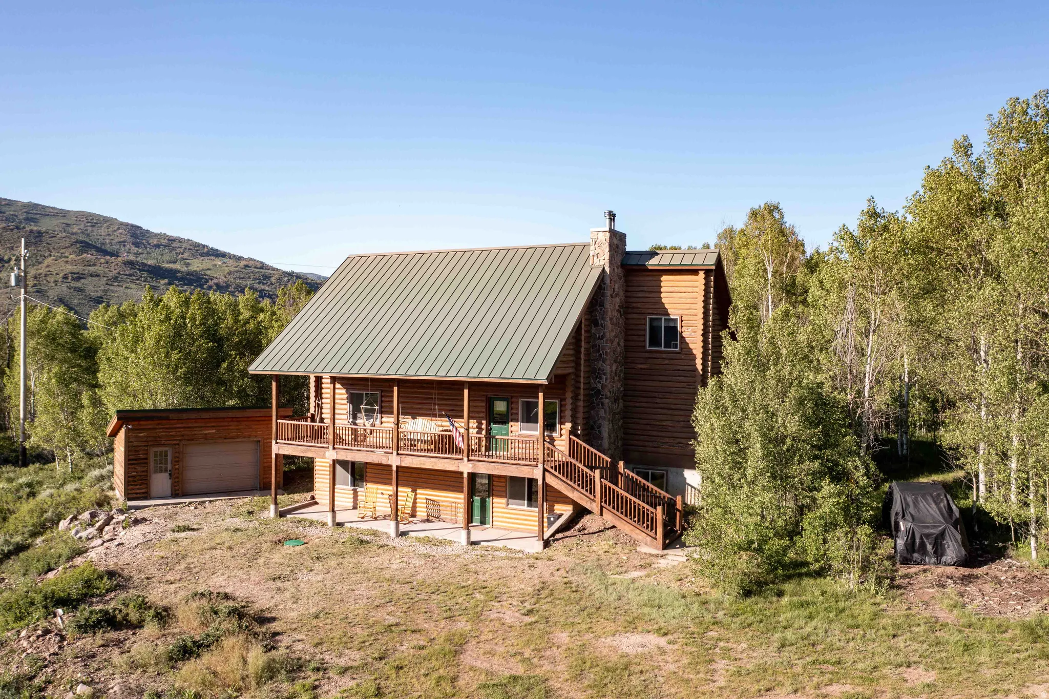 Rear view of property featuring a chimney, a deck, a detached garage, a standing seam roof, and an outbuilding