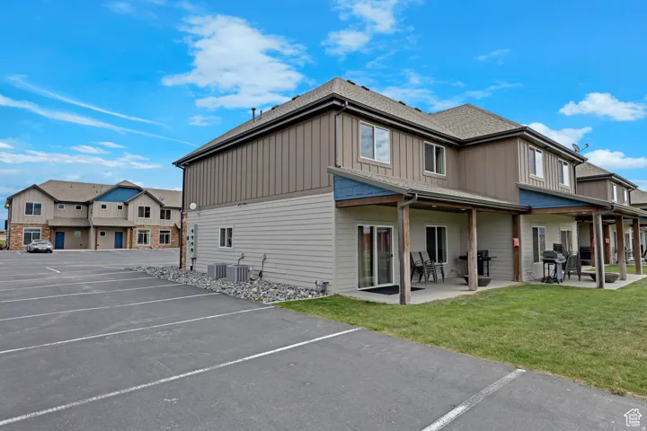 Rear view of house featuring uncovered parking, board and batten siding, a lawn, and a patio