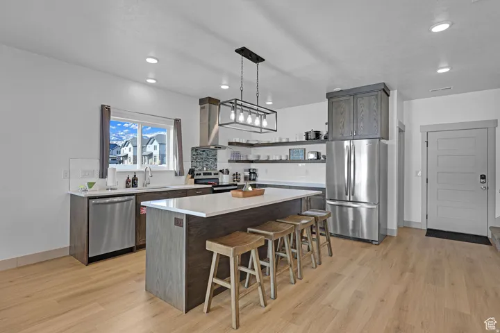 Kitchen with stainless steel appliances, decorative light fixtures, a kitchen island, and light wood-type flooring