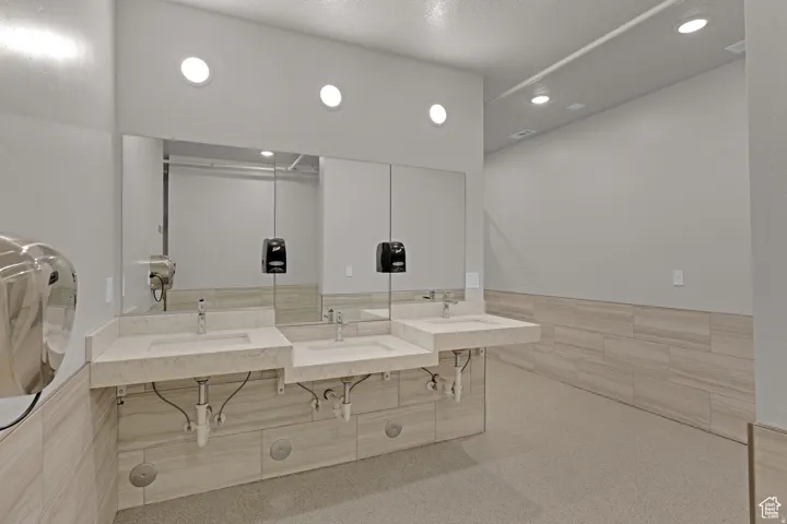 Bathroom with double vanity, tile walls, recessed lighting, and a wainscoted wall