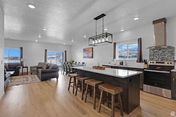 Kitchen with electric stove, a breakfast bar, backsplash, island range hood, and a kitchen island