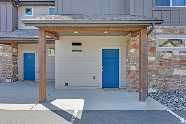 Property entrance featuring board and batten siding, stone siding, a shingled roof, and a porch